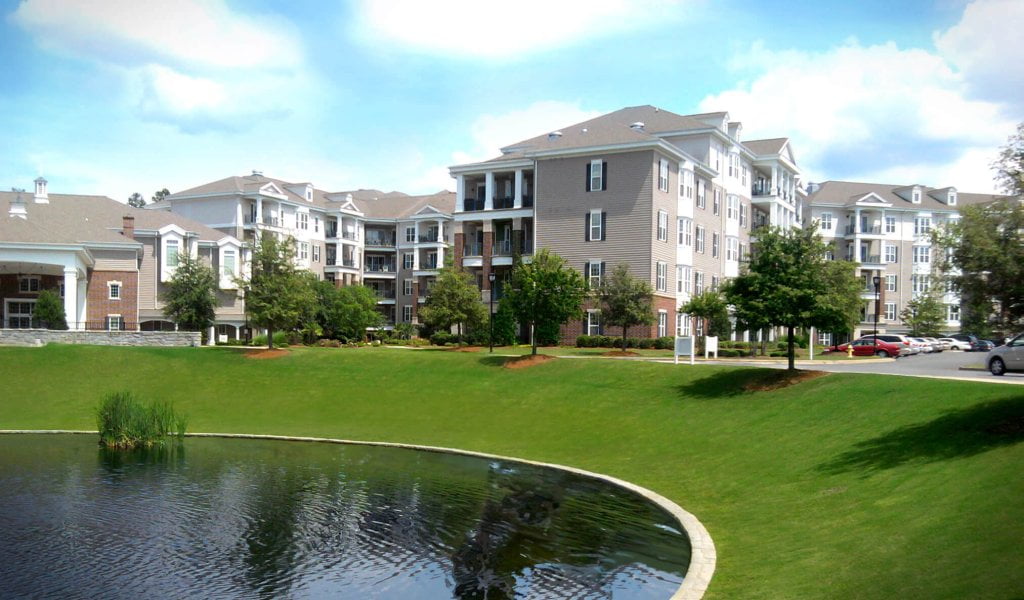 The green grass and pond in front of the big houses.
