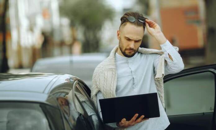 A man standing next to his car with a laptop.