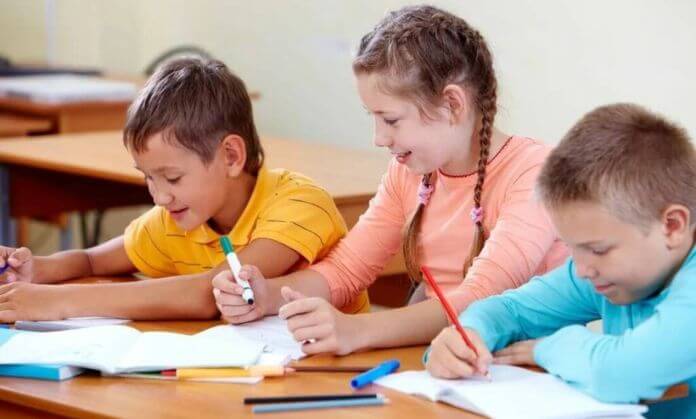 children are sitting at a table and writing.