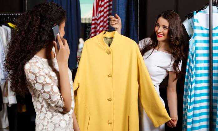 two girls smiling and one of them holding a yellow coat 