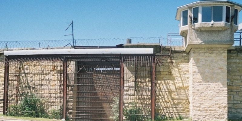 a fenced in wall with a house behind it 